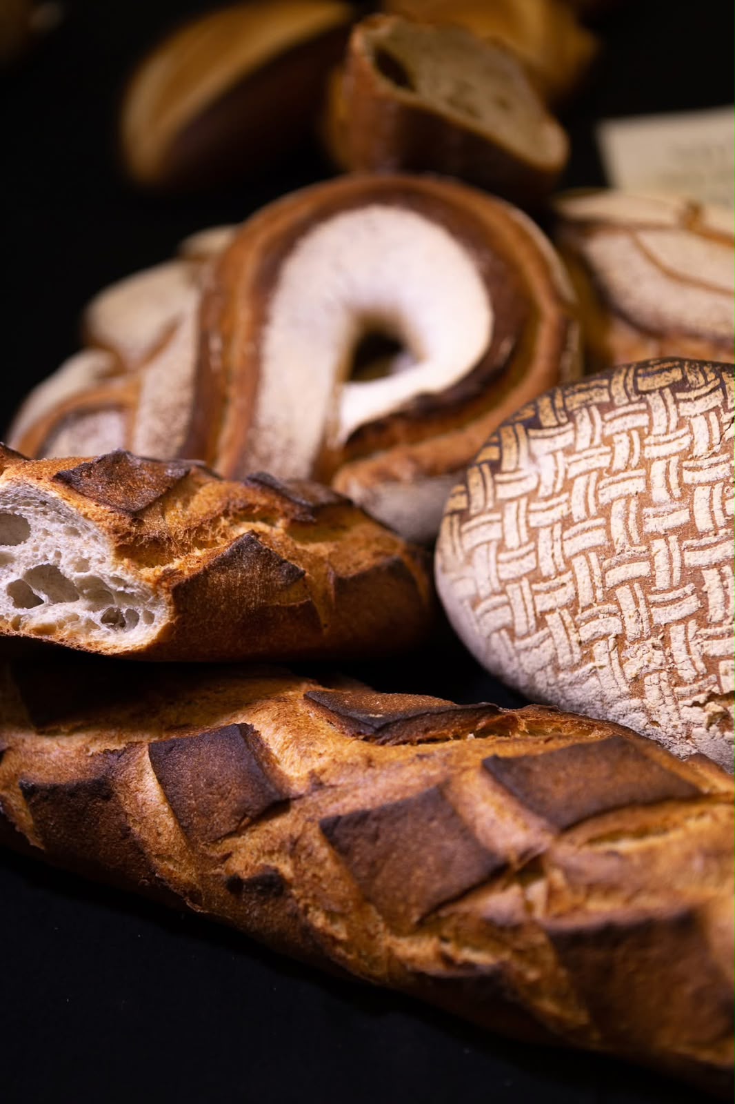 Pains artisanaux aux croûtes scarifiées et boule décorée d'un tressage de farine, sur fond noir
