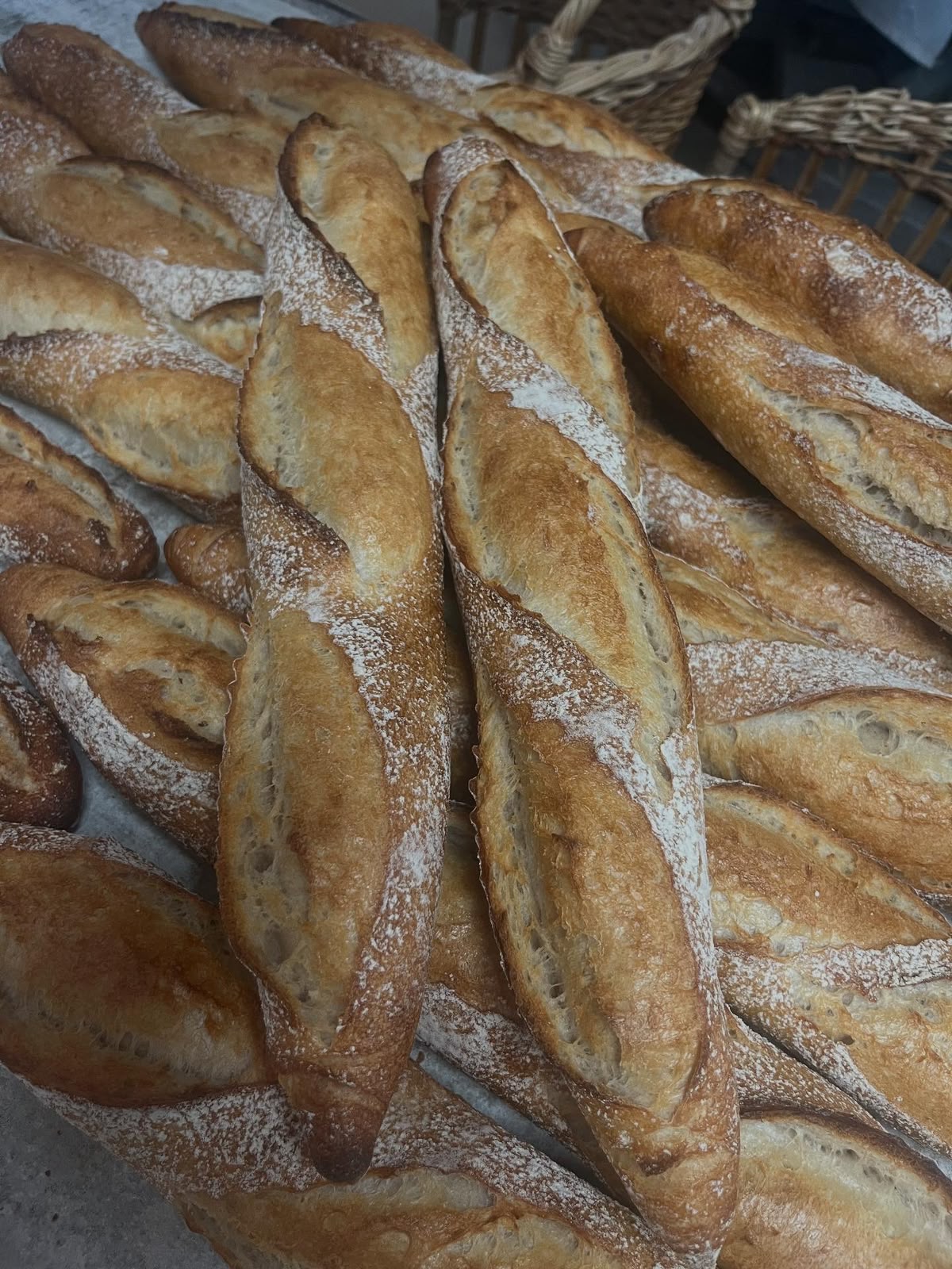 Baguettes dorées et farinées, alignées devant des paniers en osier