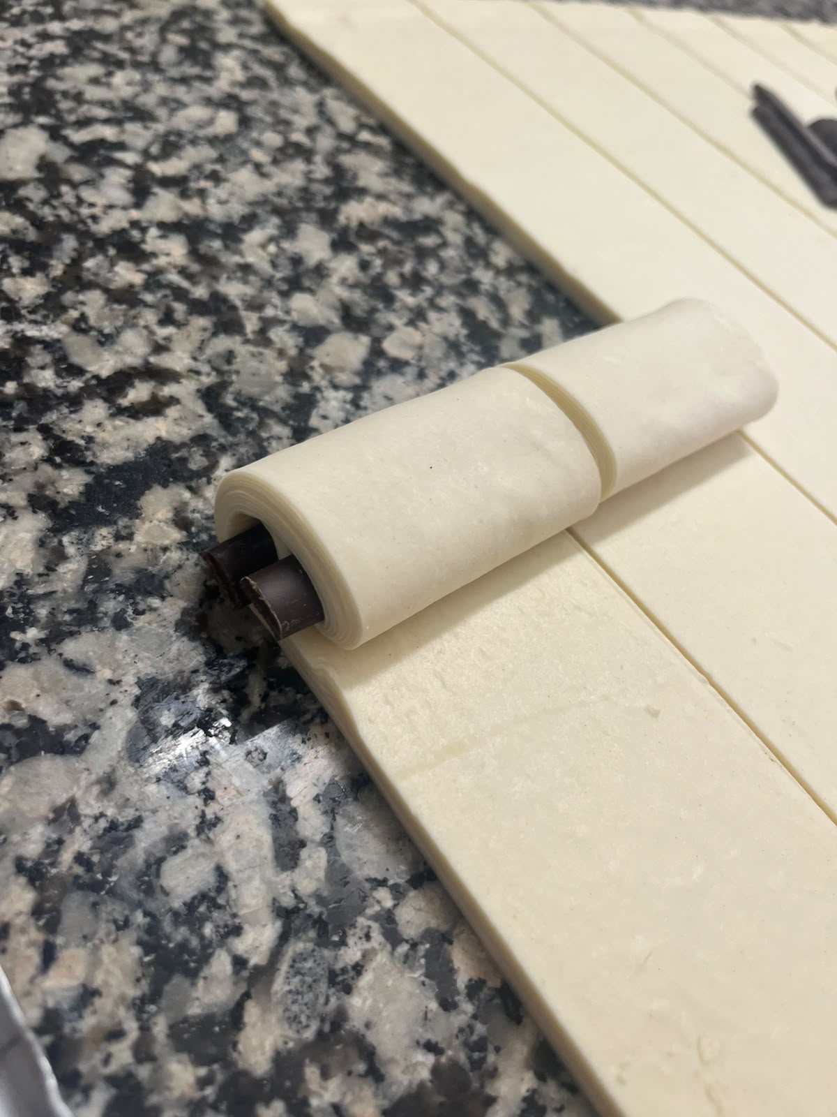 Mains du boulanger roulant la pâte feuilletée autour des barres de chocolat, sur le plan de travail