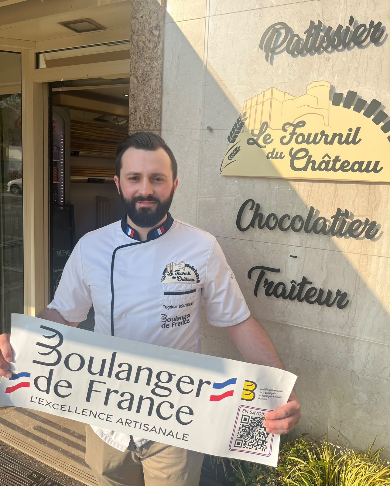 Tugdual Boutillier devant la devanture de la boutique, tenant la banderole « Boulanger de France »