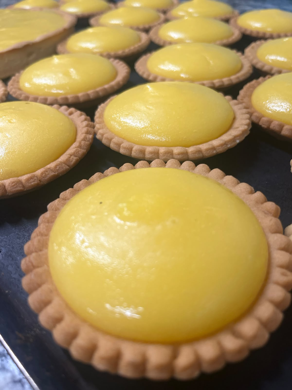 Tartelettes au citron à la crème bombée et brillante, alignées sur plaque au fournil