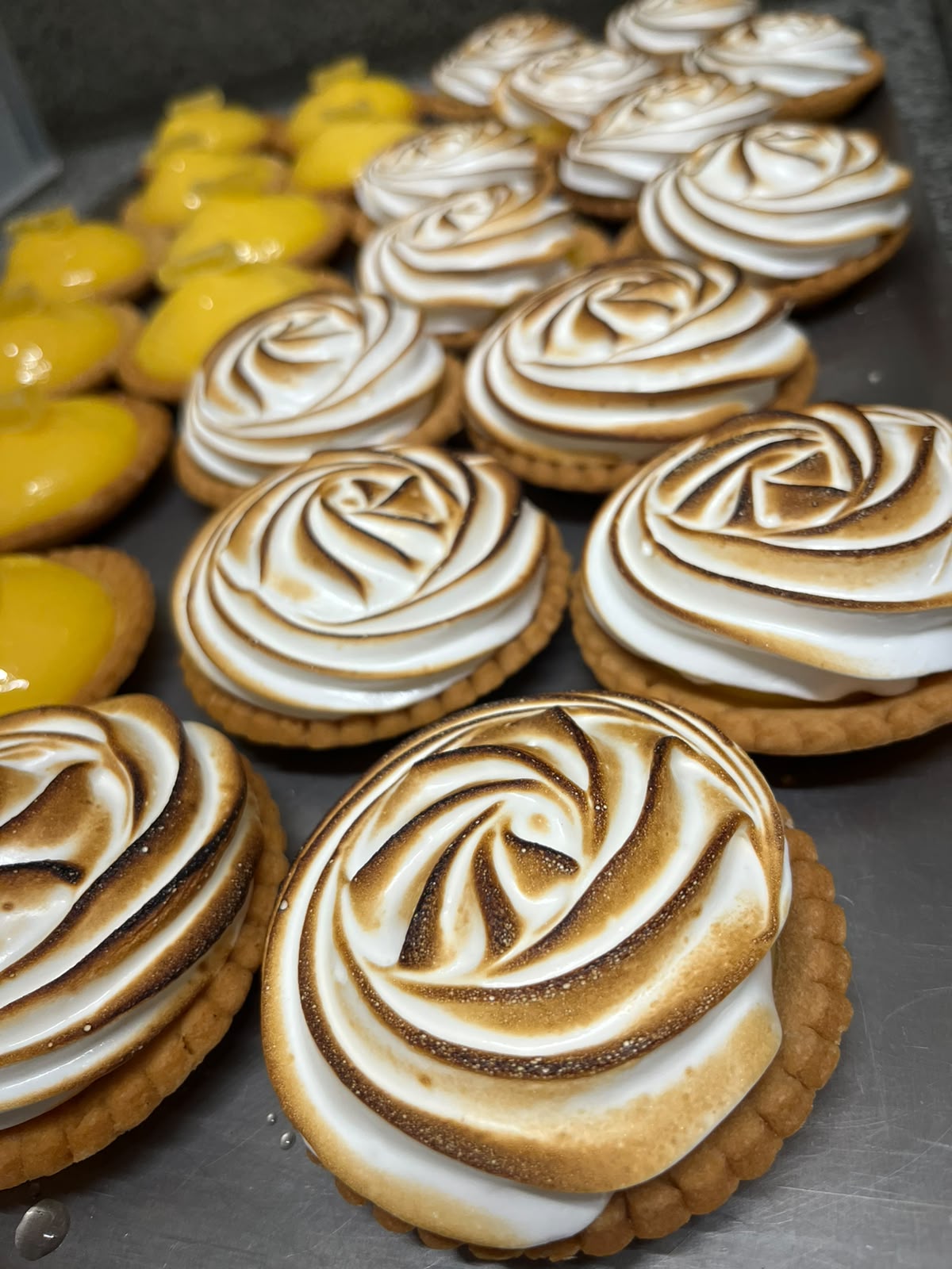 Tartelettes meringuées en rosaces dorées au chalumeau, tartelettes au citron en arrière-plan
