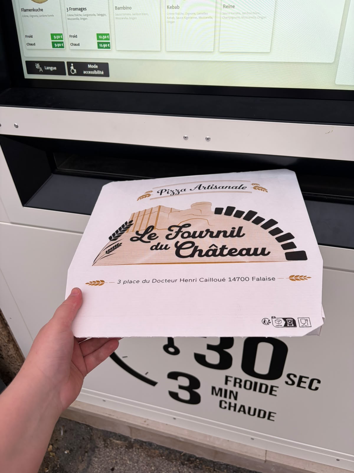 Boîte à pizza Le Fournil du Château tenue devant l'écran du distributeur automatique