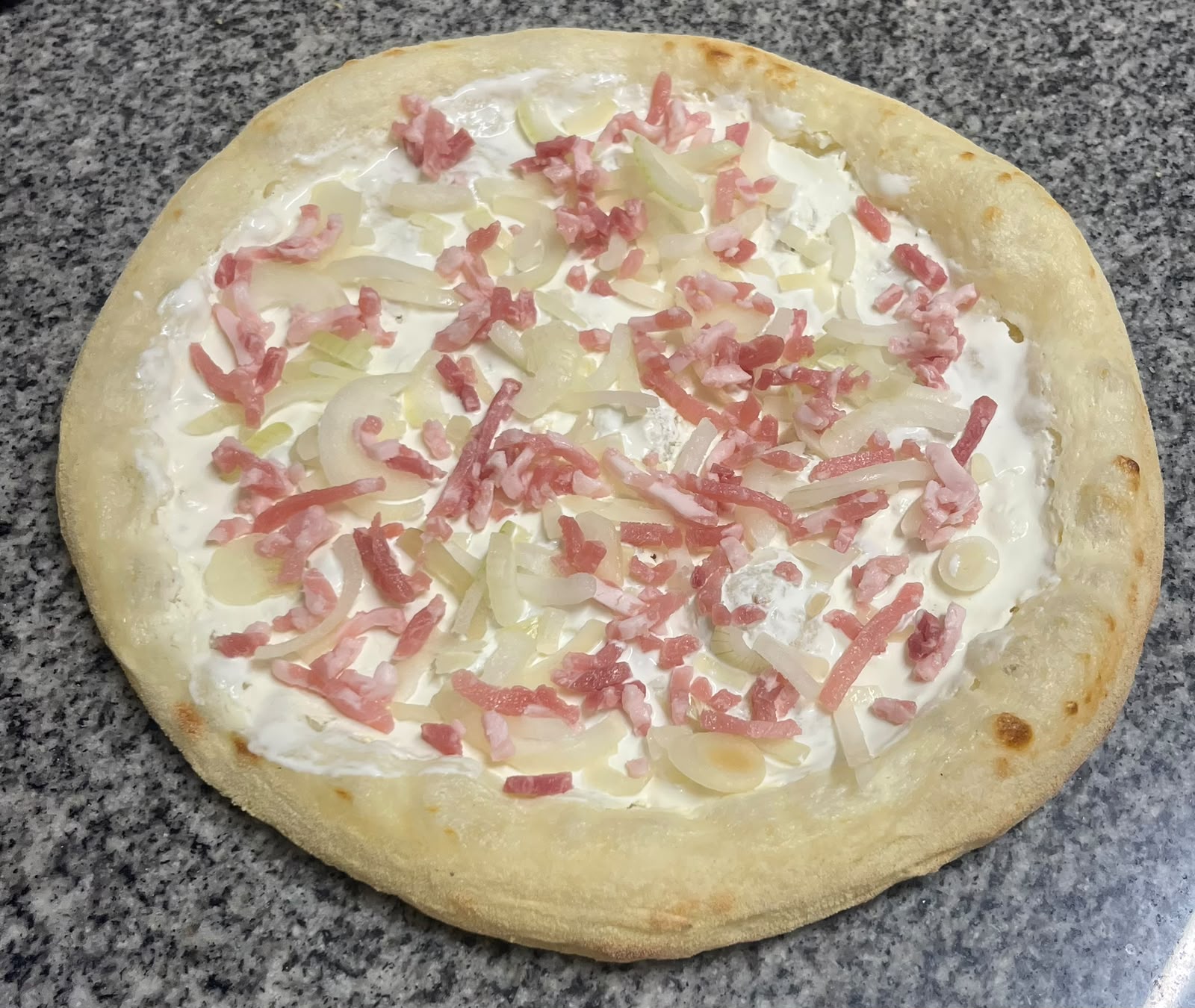 Flamenkuche crue : crème, oignons émincés et lardons fumés, garnie au fournil