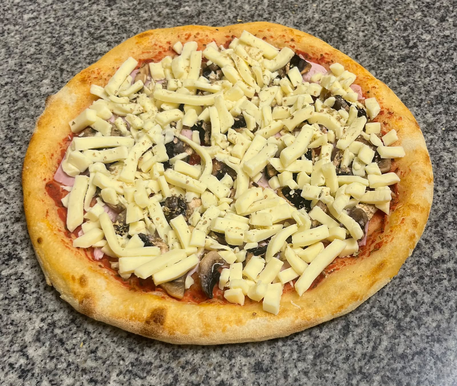 Pizza reine crue : sauce tomate, jambon blanc, champignons et mozzarella, garnie au fournil