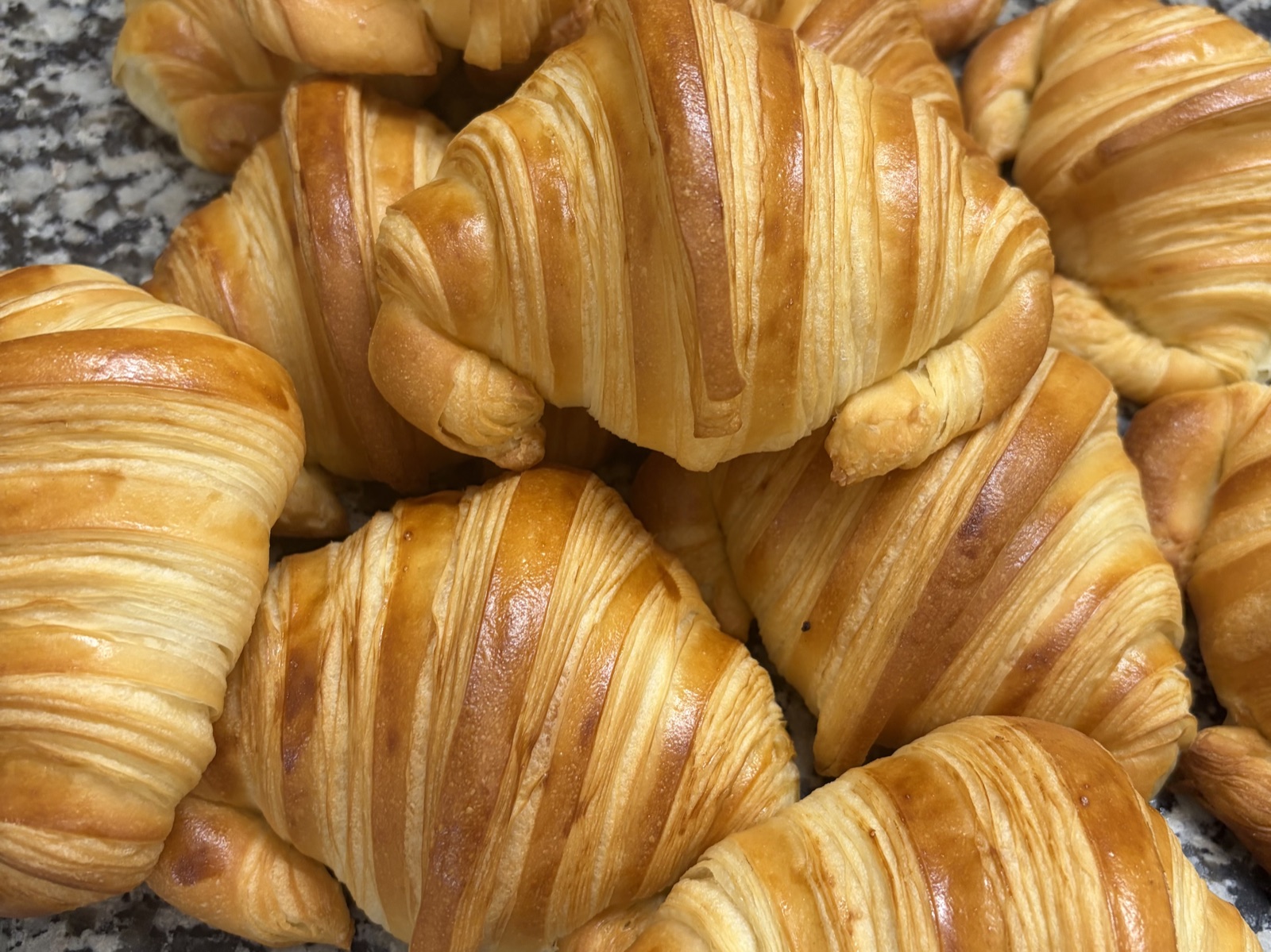 Croissants dorés au feuilletage marqué, empilés sur un plan de travail en granit